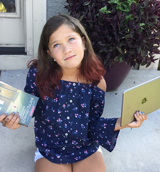 Girl holding a book in one hand and a tablet computer in the other.