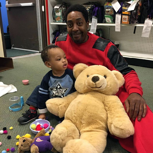 A man and his son sitting with toys and a large teddy bear