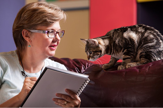 Kathi Appelt writing in a notebook while a cat watches