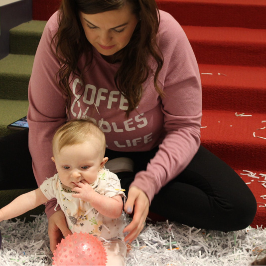 Baby Adellayde explores shredded paper with her mom in play pit.