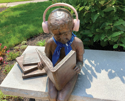 Melrose (MA) Public Library’s bronze Little Reader statue was created by artist Carolyn Wirth in 1999. For more on the library’s podcast book club, see page 34. 