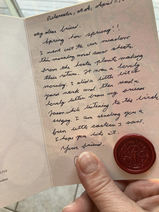 A hand holds a hand-written greeting card with a red wax seal.